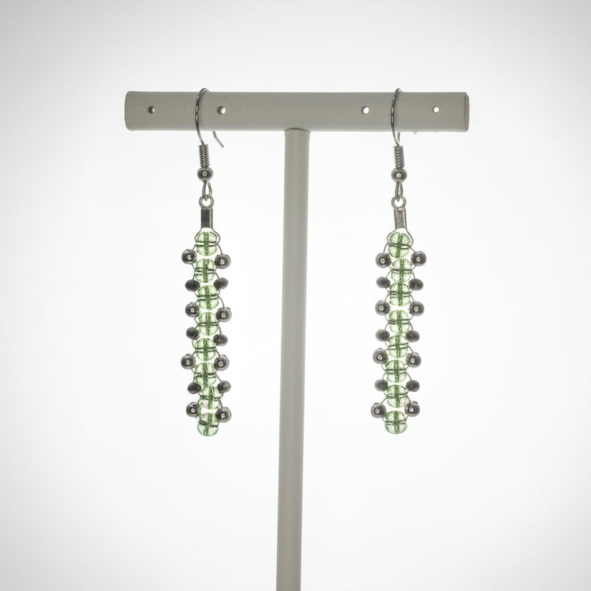 Pair of green beaded earrings on a white stand against a white background