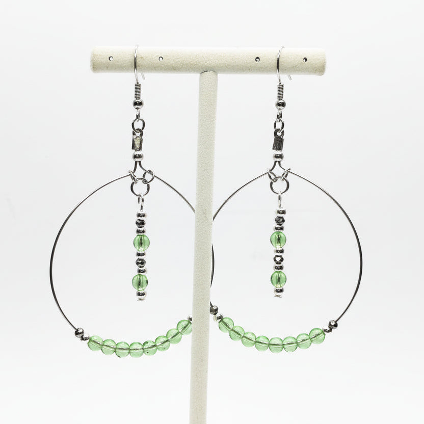 Hoop earrings with green beads on a white stand against a white background