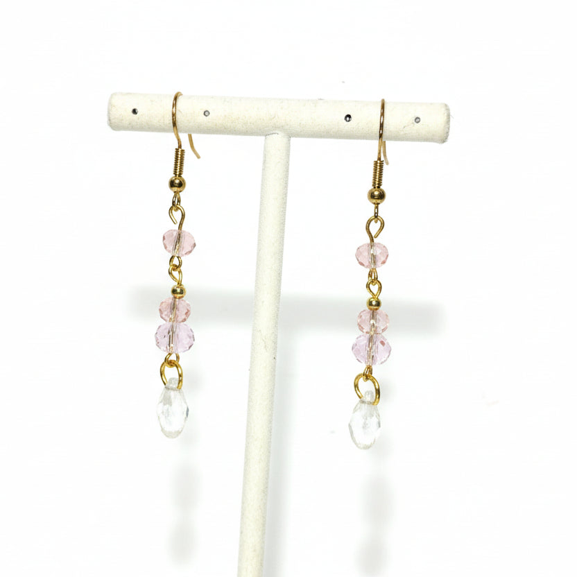 Pair of earrings with pink and clear beads on a white stand against a white background