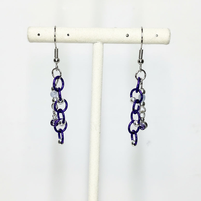 Pair of blue chainmaille earrings on a white stand against a white background