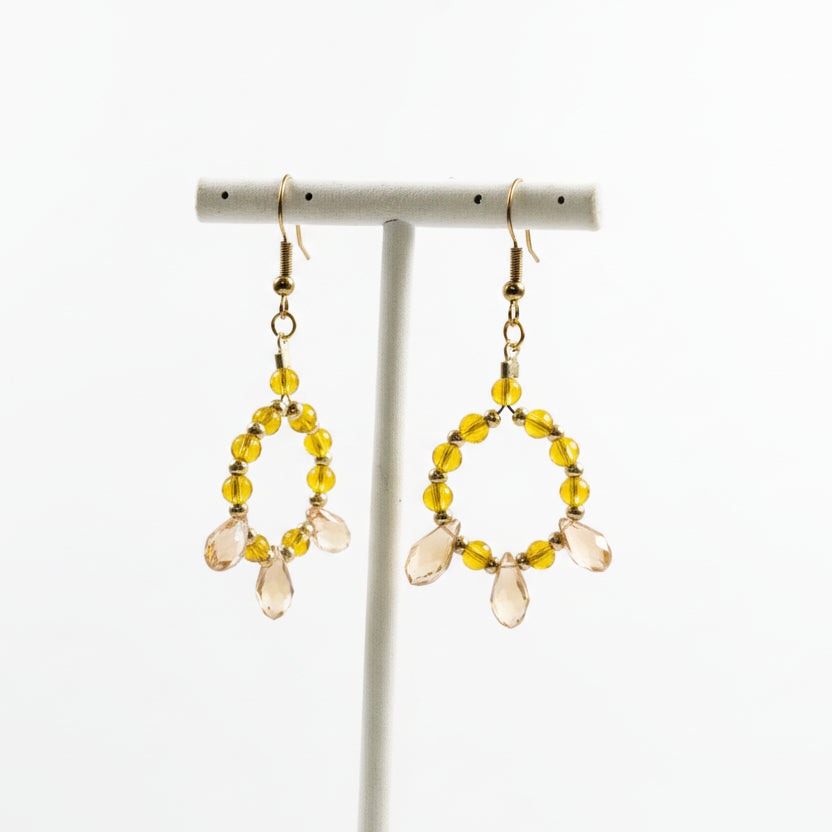 Pair of gold earrings with yellow beads on a white stand against a white background