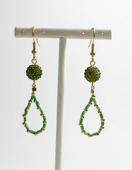Green beaded earrings on a white stand against a white background