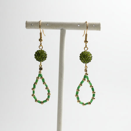 Green beaded earrings on a white stand against a white background